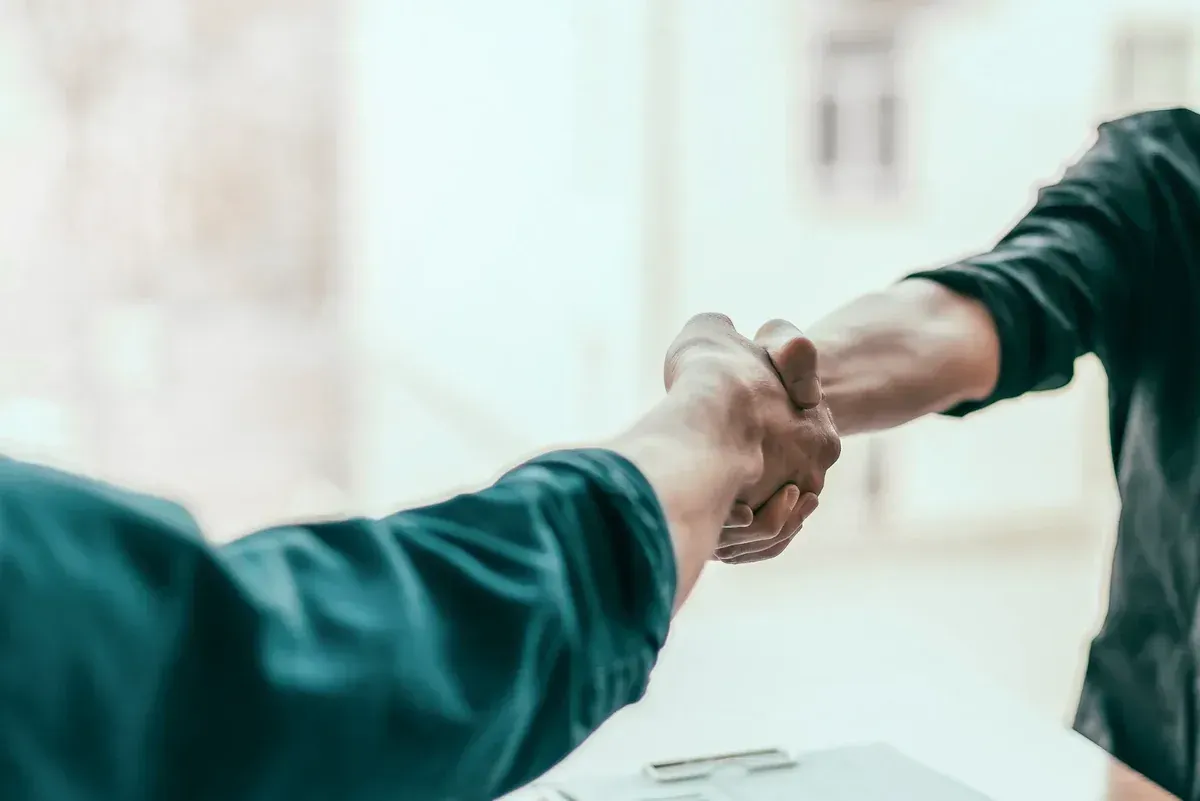 Dos personas dándose la mano, fondo borroso, primer plano.