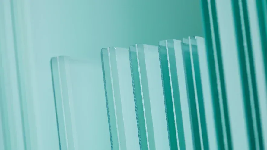 Pilhas de painéis de vidro transparente, de espessuras variadas, em tons de verde-azulado.