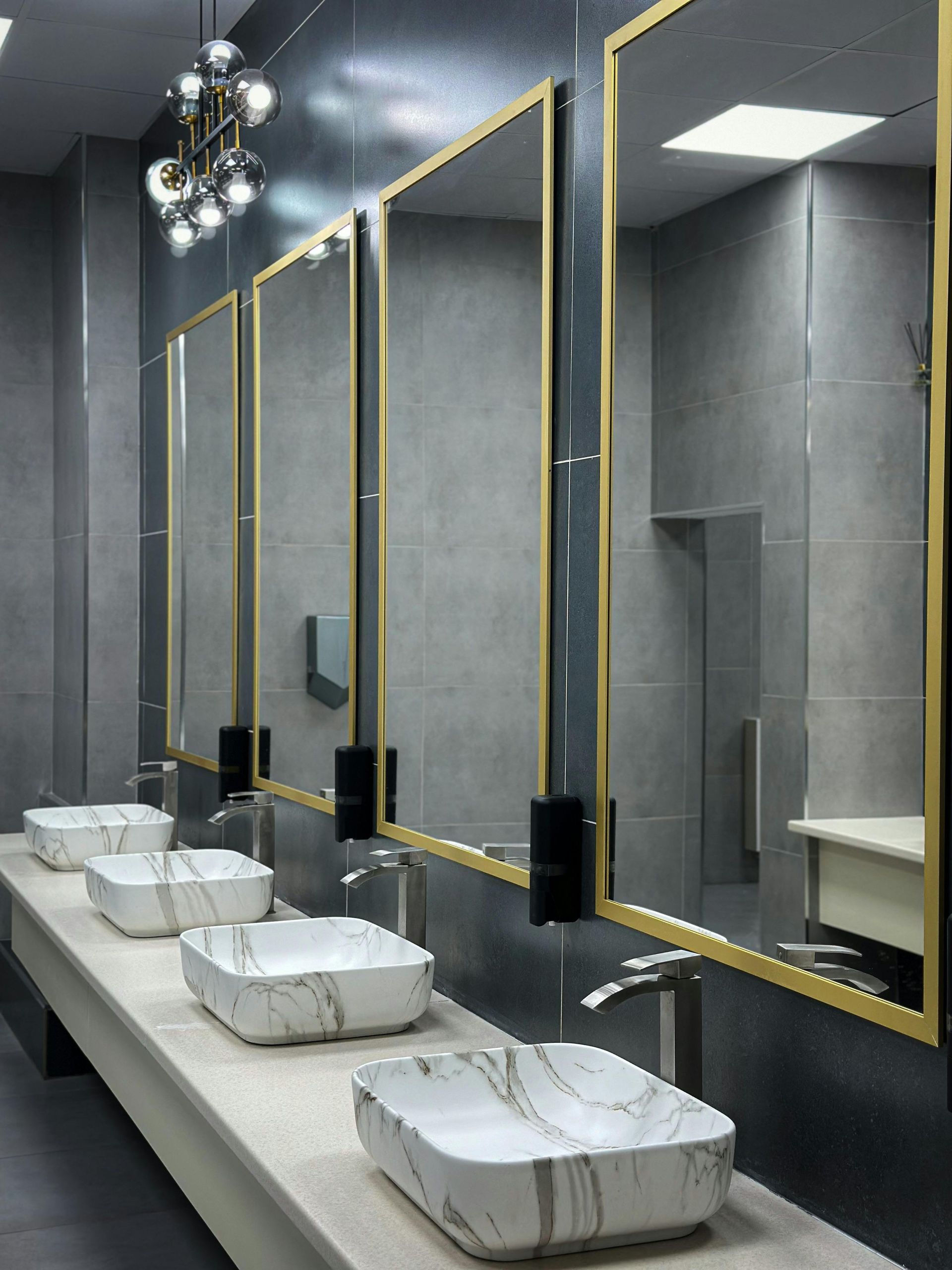 Banheiro moderno com pias de mármore, espelhos com moldura dourada e paredes cinza.