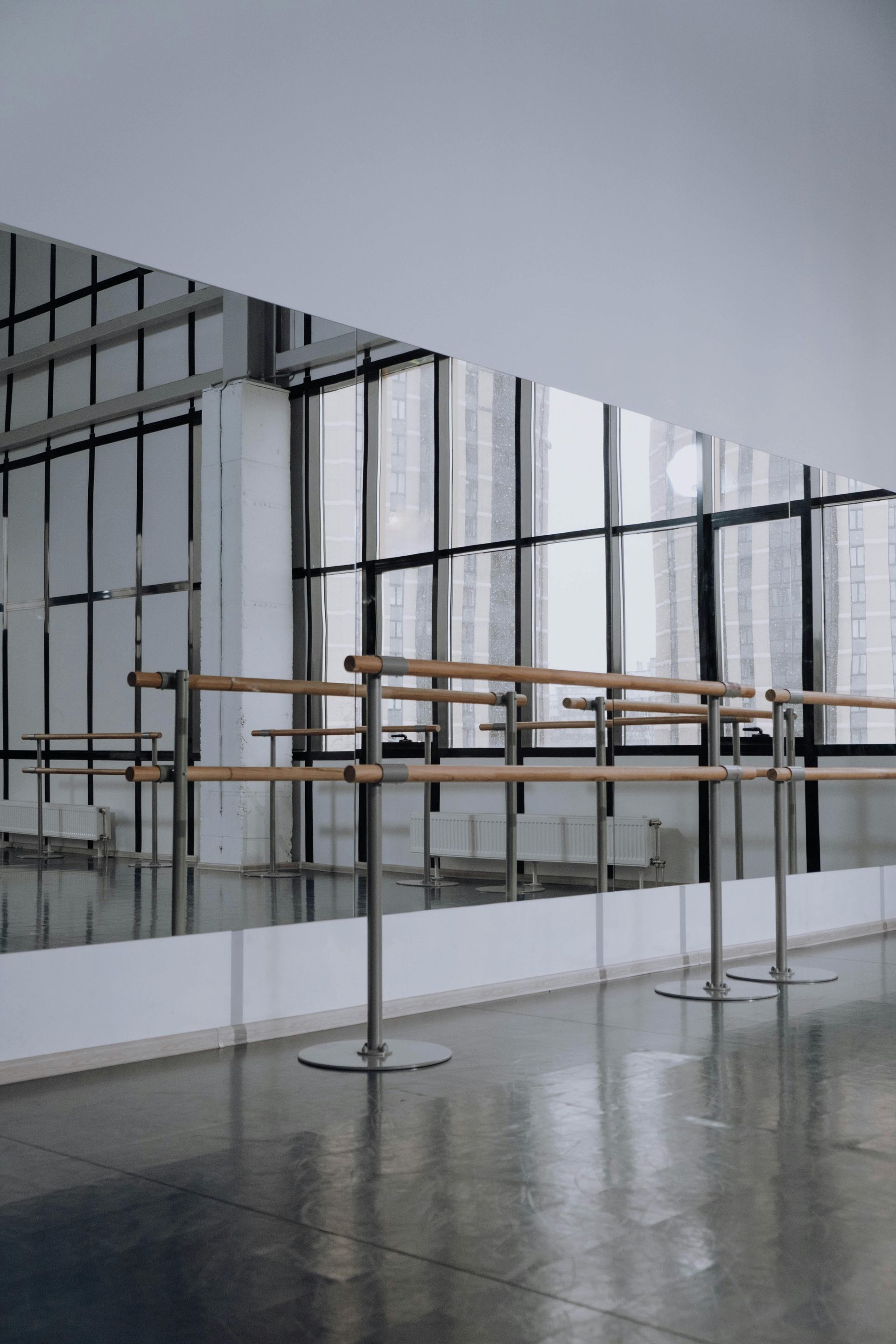 Estúdio de dança vazio com barras de balé e grandes espelhos que refletem janelas e vista para o exterior.