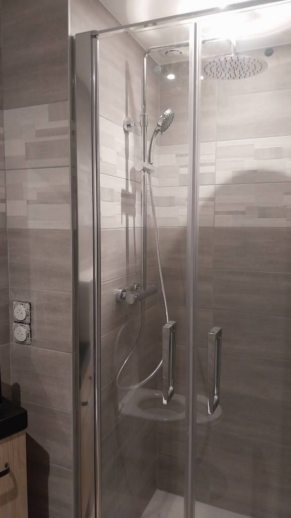 Cabine de douche avec portes vitrées, luminaires argentés et murs carrelés