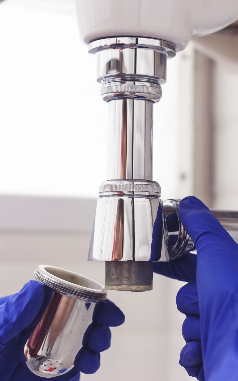 Des mains gantées de bleu dévissent un appareil de plomberie