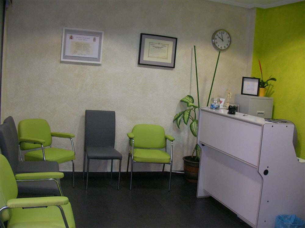 Una sala de espera con sillas verdes y un reloj en la pared.