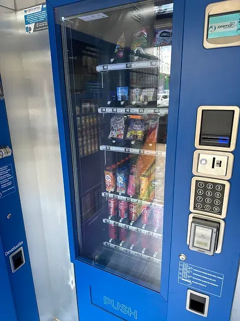 Una máquina expendedora azul llena de bocadillos y bebidas.