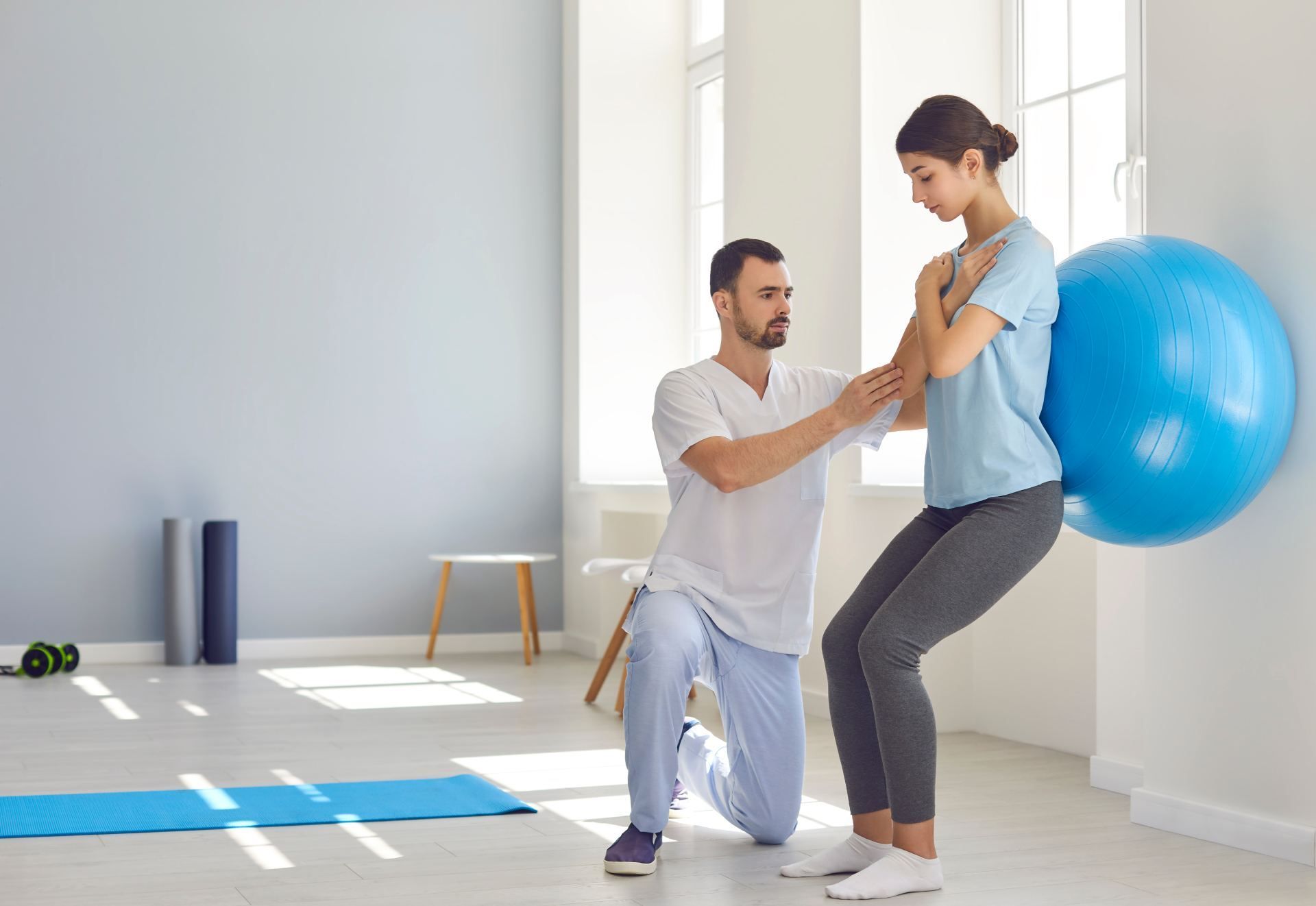 Ein Mann hilft einer Frau, mit einem blauen Gymnastikball in die Hocke zu gehen.