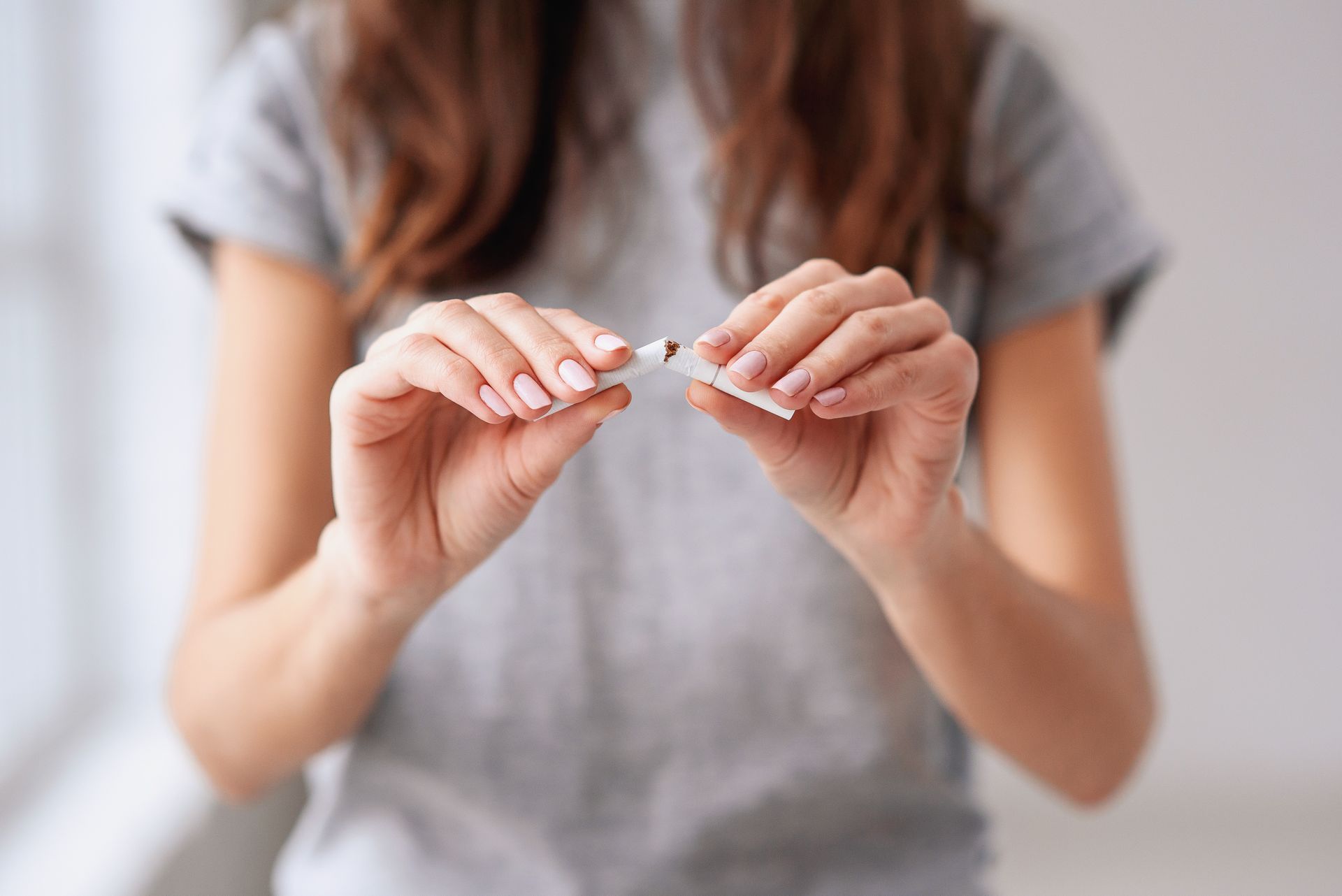 Une femme en chemise grise casse une cigarette blanche en deux, à l'intérieur.