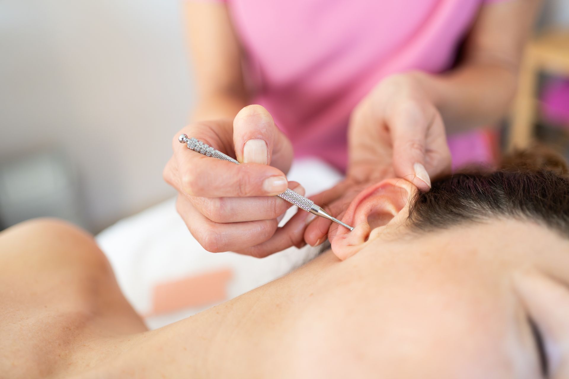 Personne recevant une séance d'acupuncture à l'oreille ; gros plan sur une main tenant une aiguille d'acupuncture.