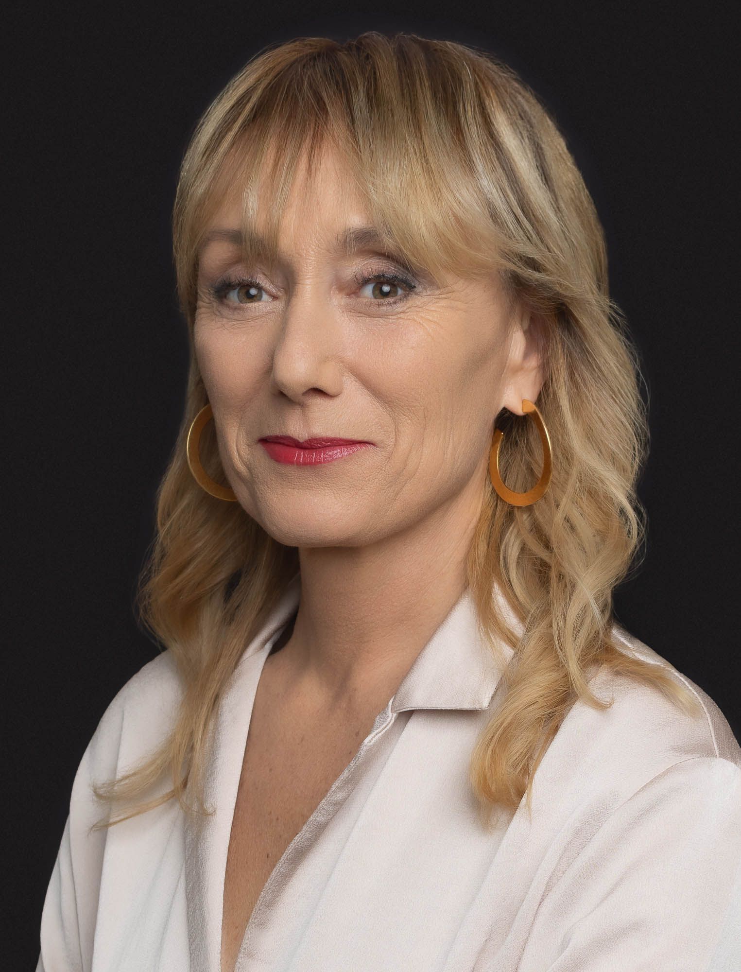 Femme aux cheveux blonds portant des boucles d'oreilles créoles en or, regardant l'objectif.