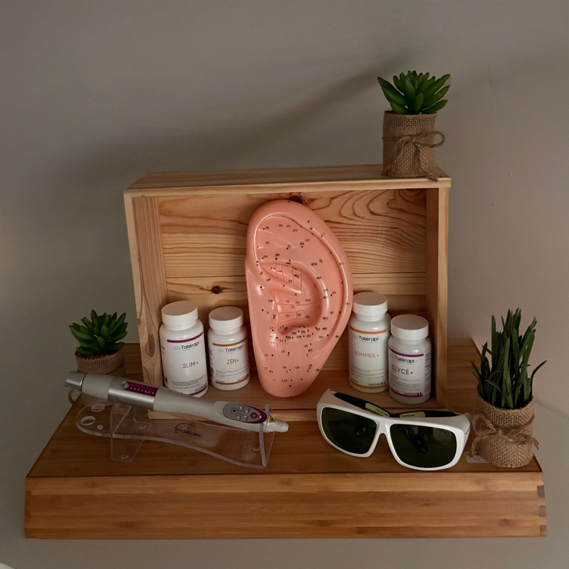 Une vitrine avec une oreille, des compléments alimentaires, un laser, des lunettes et des plantes sur des étagères.