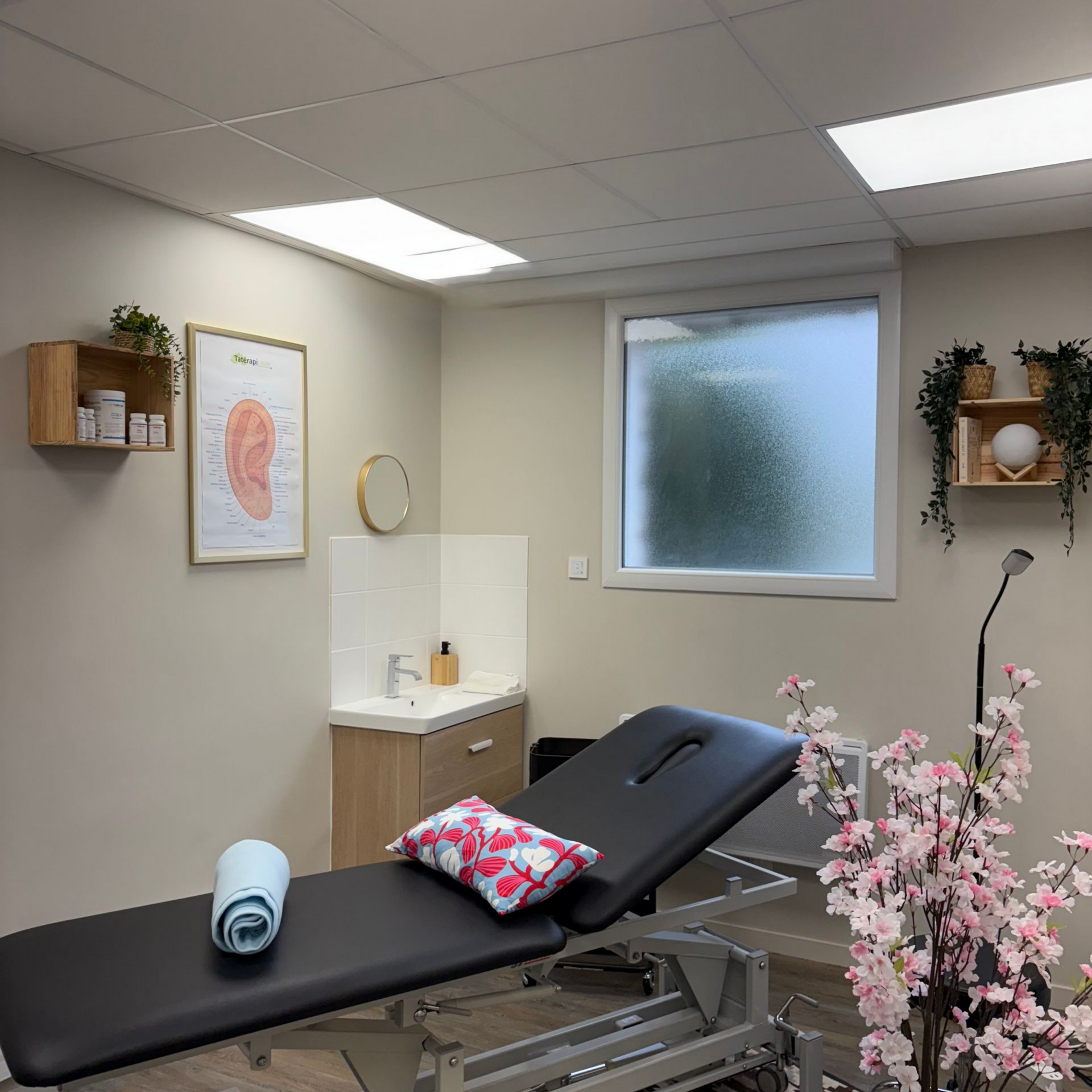 Salle de massage avec table de massage, lavabo, fenêtre et plantes décoratives.