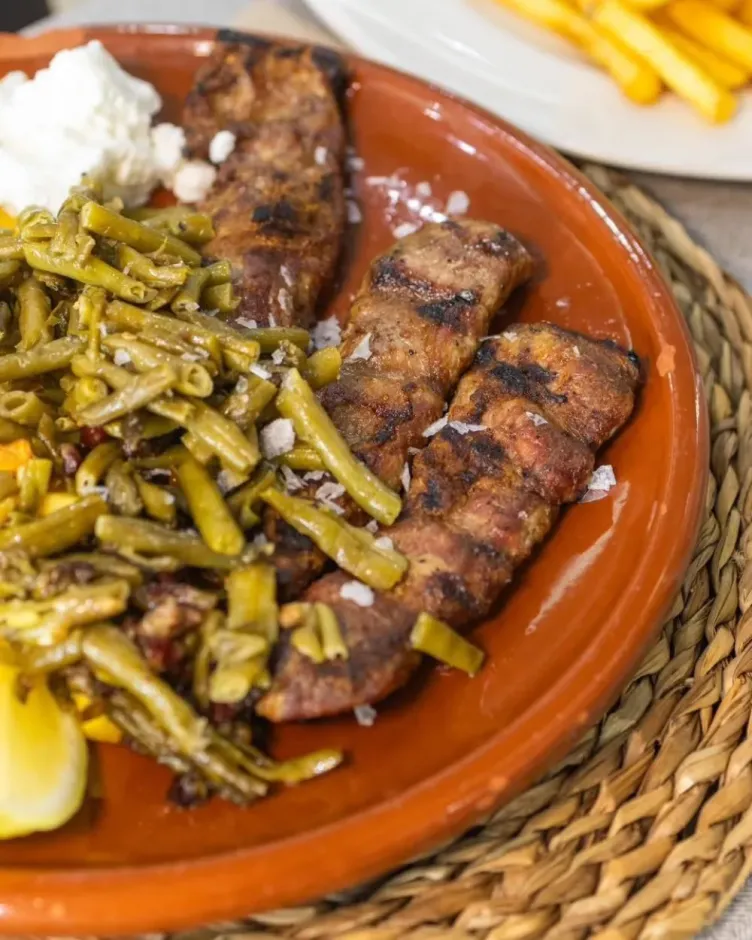 Carne a la parrilla con judías verdes, una cucharada de salsa blanca y una rodaja de limón en un plato de terracota.