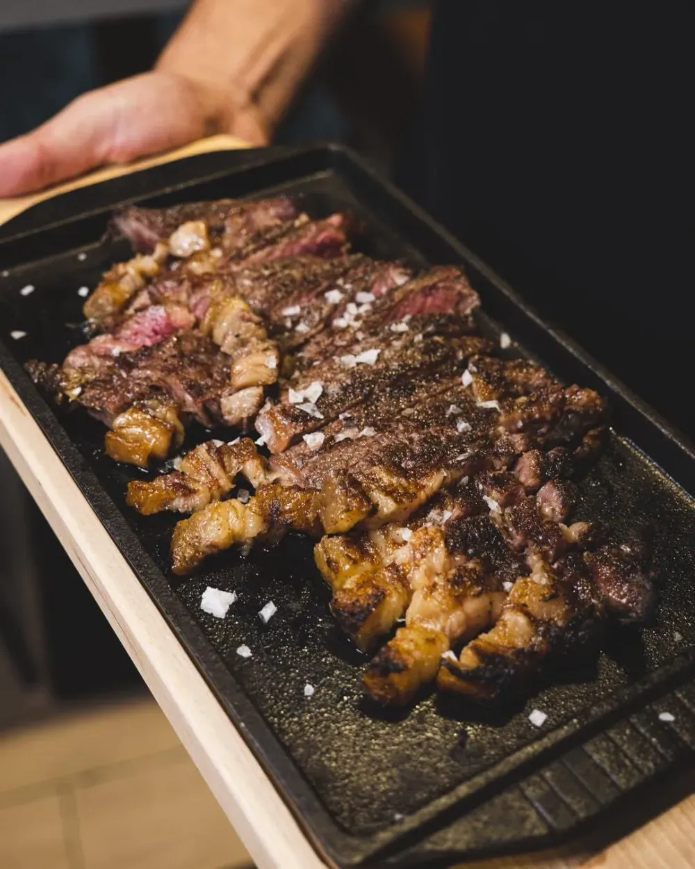 Filete a la parrilla rebanado sobre una plancha de hierro fundido negro, espolvoreado con sal. Sostenido por una persona.