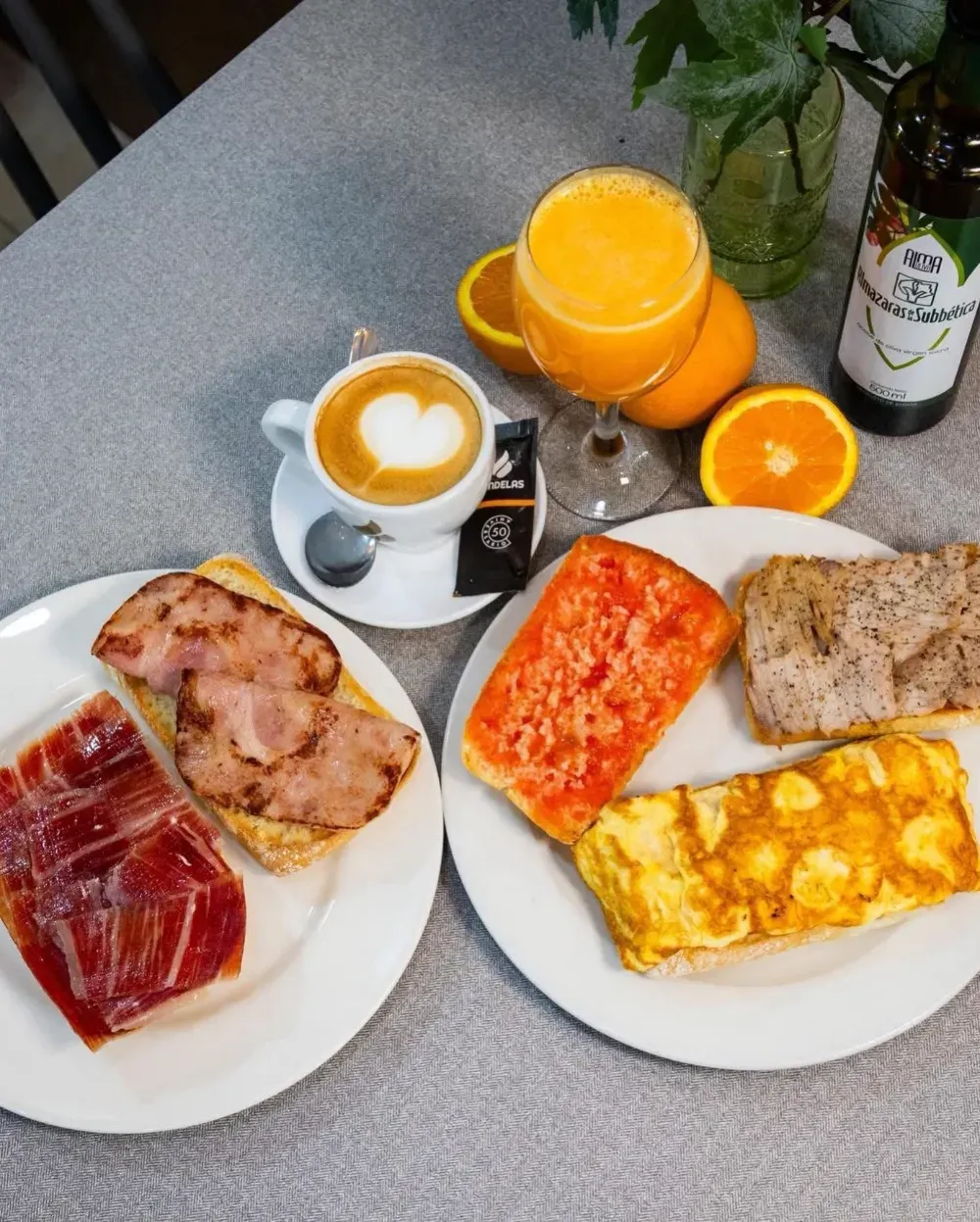 Desayuno: tostadas con jamón, tomate y tortilla, café con arte de corazón, zumo de naranja, naranjas.