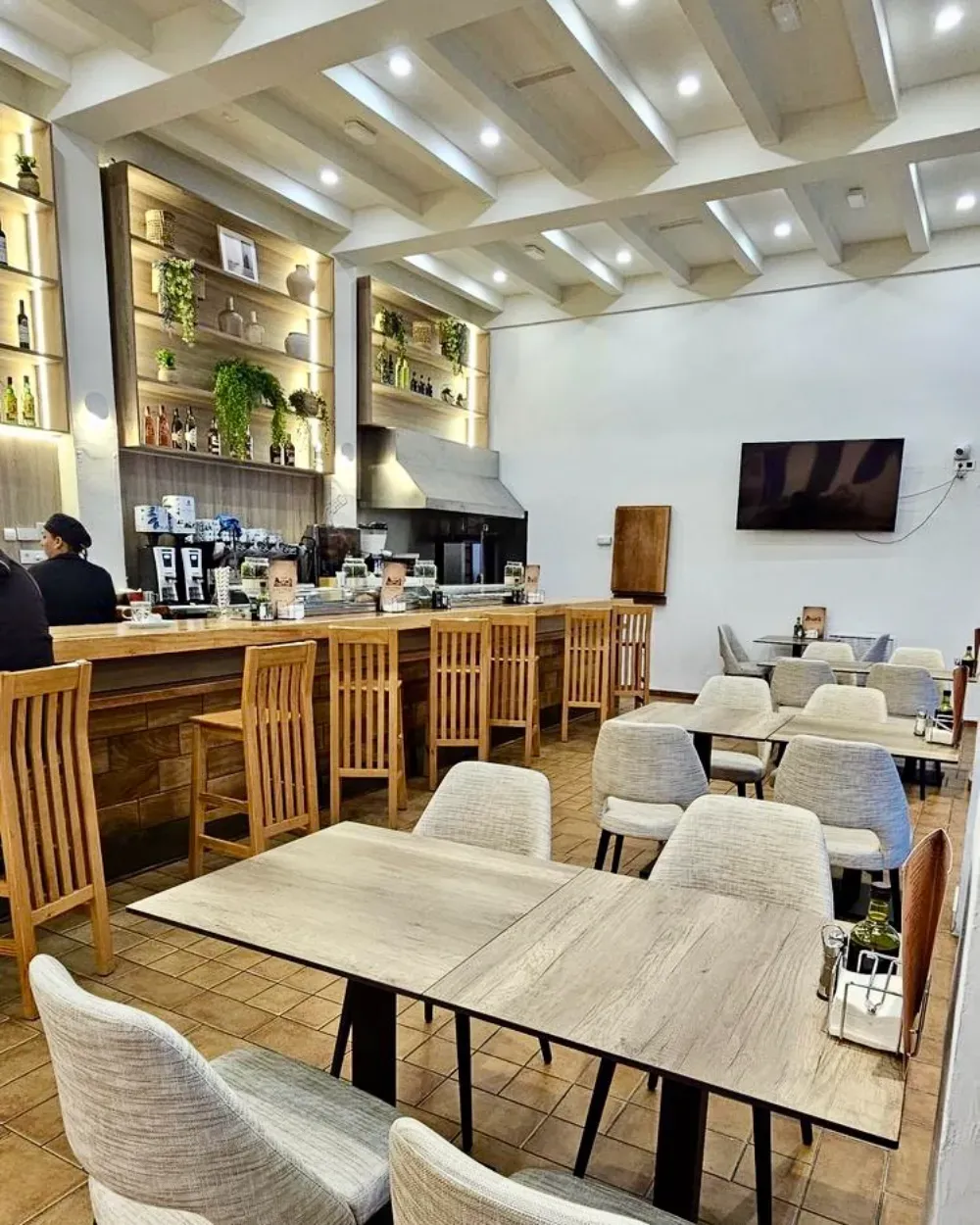 Interior de cafetería con barra de madera, mesas, sillas y estanterías.