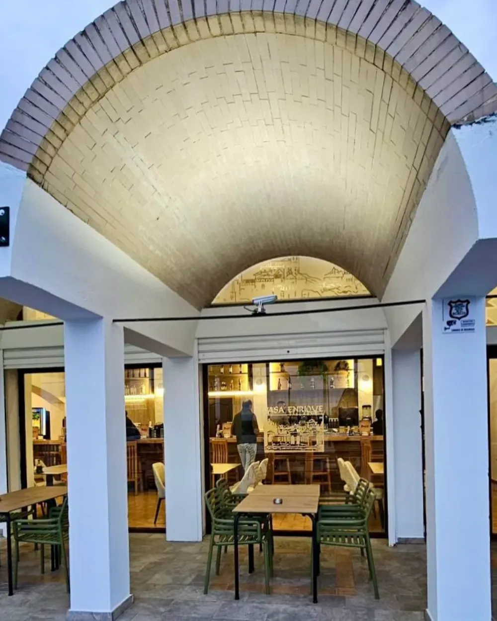 Patio del restaurante con techo abovedado, mesas y vista al interior con una persona de pie.