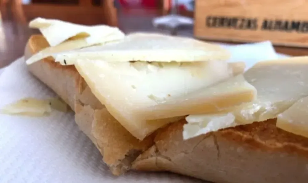Pan con queso en lonchas sobre una servilleta blanca. Letrero de madera al fondo.