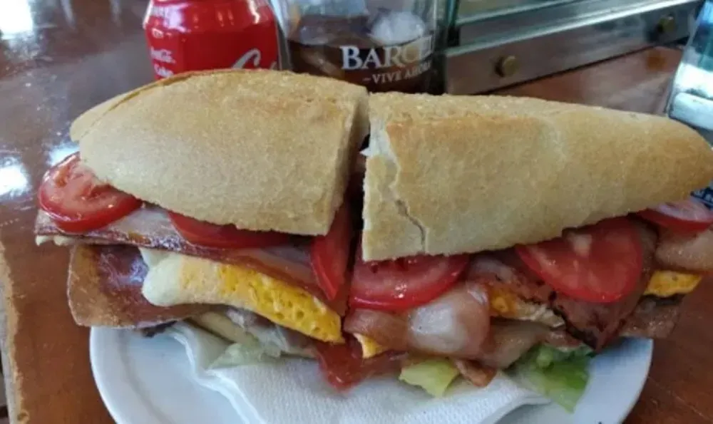 Sándwich grande cortado por la mitad con tocino, huevo, tomate y lechuga en un plato blanco.