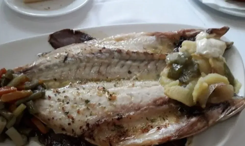 Pescado a la parrilla en un plato blanco con verduras; toma cenital.