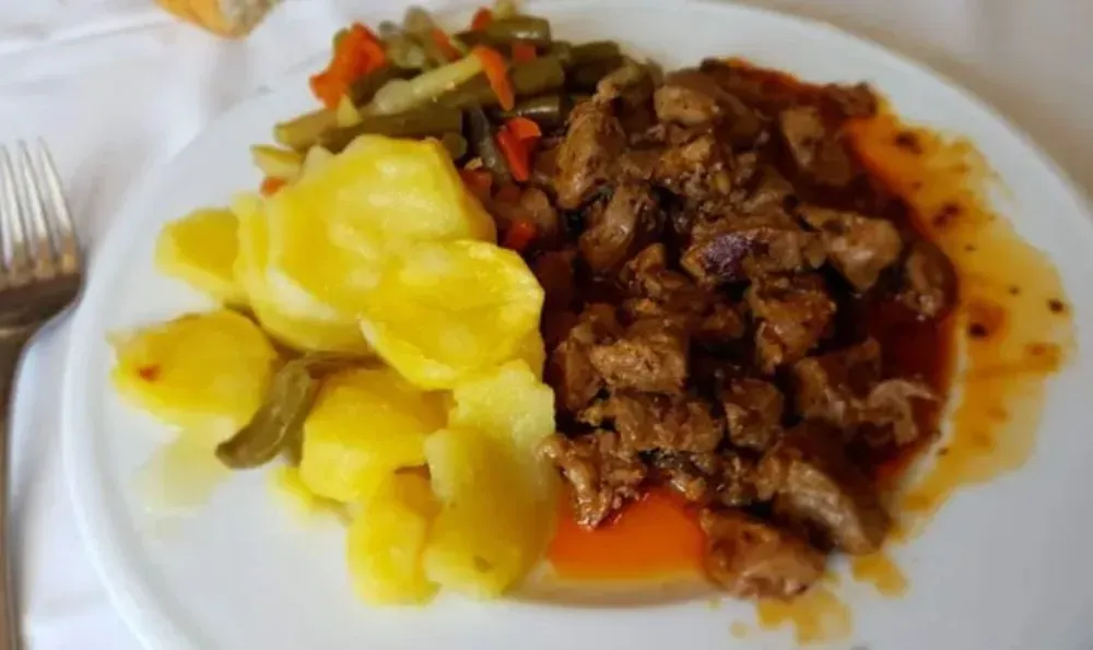 Plato con trozos de carne en salsa, patatas cocidas y verduras mixtas.