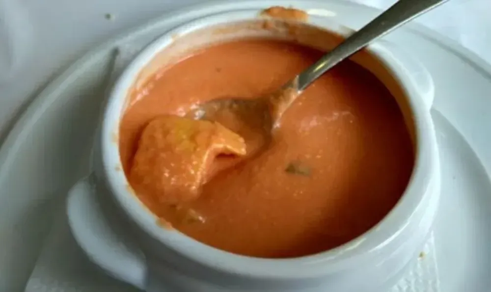 Sopa cremosa de naranja en recipiente blanco con mango y cuchara.