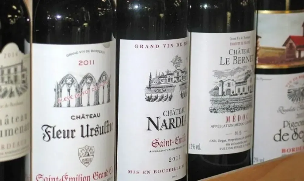 Primer plano de varias botellas de vino tinto con diferentes etiquetas, incluidas Château Fleur Ursulines y Château Nardau.