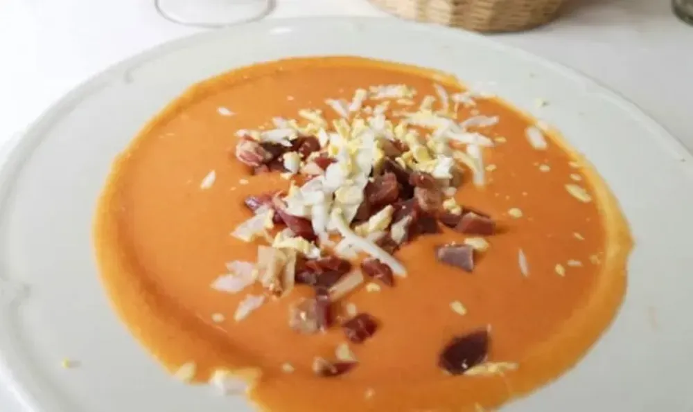 Sopa de gazpacho cubierta con huevo picado y jamón en un plato blanco.