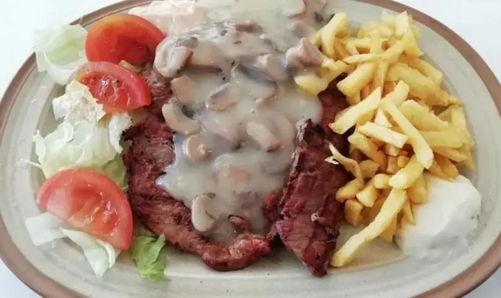 Bistec con salsa de champiñones, patatas fritas, ensalada y tomate en un plato.