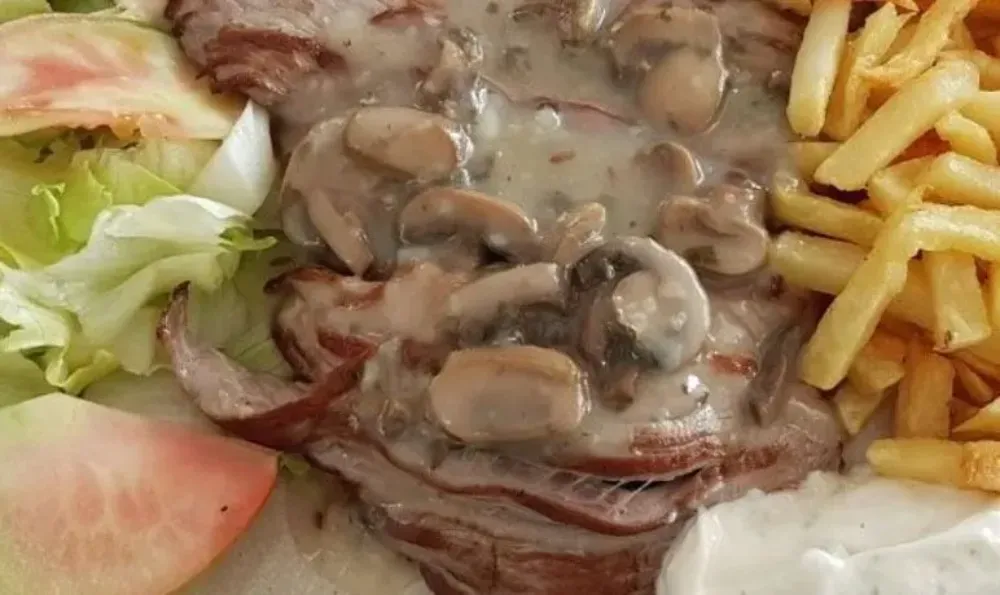 Bistec cubierto con salsa de champiñones, servido con papas fritas, lechuga y tomate.