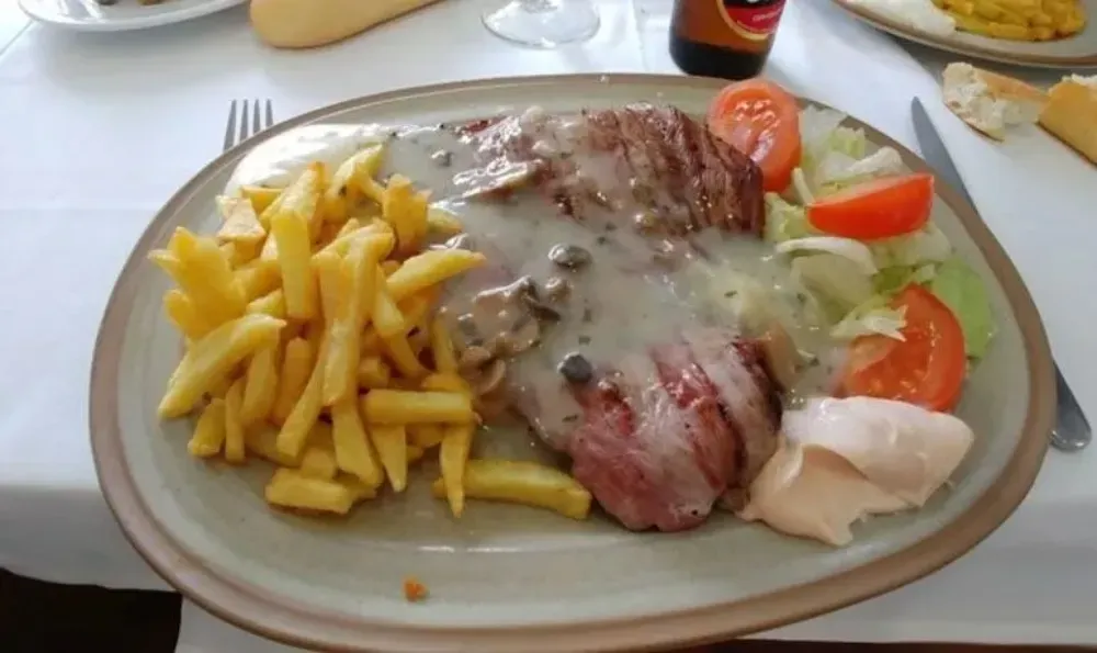 Bistec con salsa, papas fritas, ensalada y salsa en un plato.