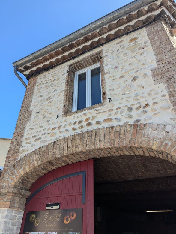 Bâtiment en pierre et en brique avec porte cintrée et porte rouge, ciel bleu.