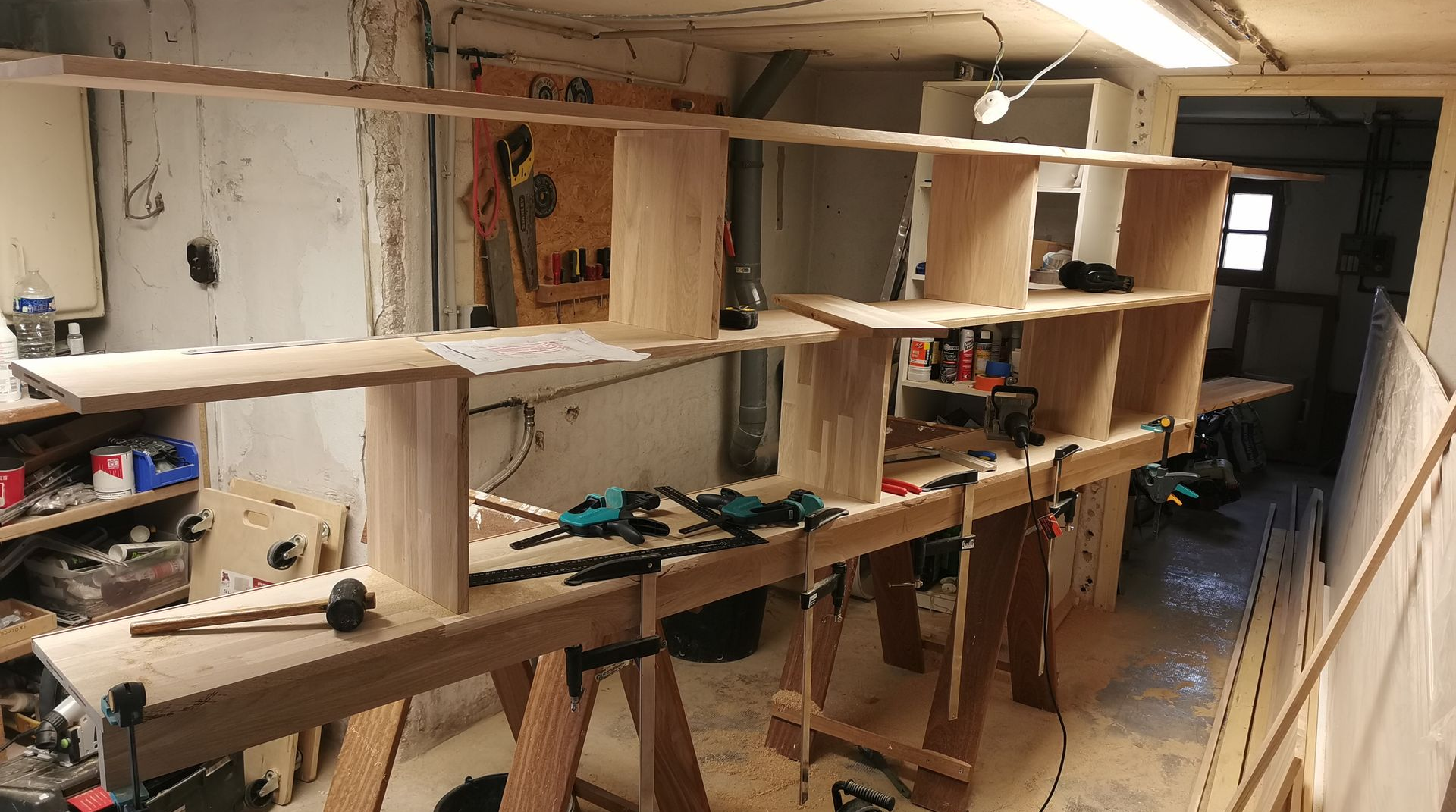 Construction d'une étagère en bois dans un atelier ; on aperçoit les étagères, les supports, les outils et les serre-joints.