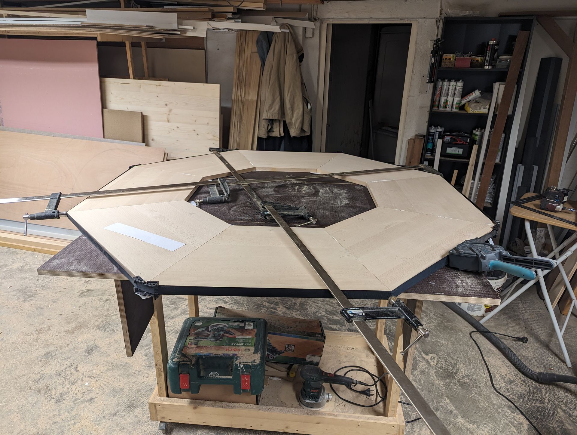 Projet de menuiserie : une grande forme en bois à plusieurs faces, fixée à une table dans un atelier.