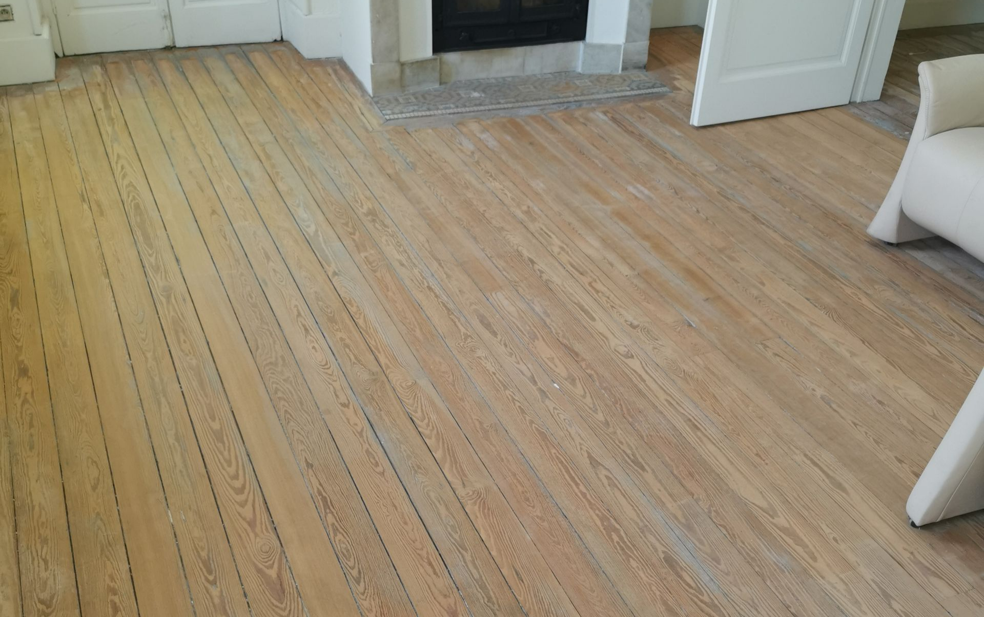 Parquet clair dans une pièce avec cheminée et meubles partiellement visibles.