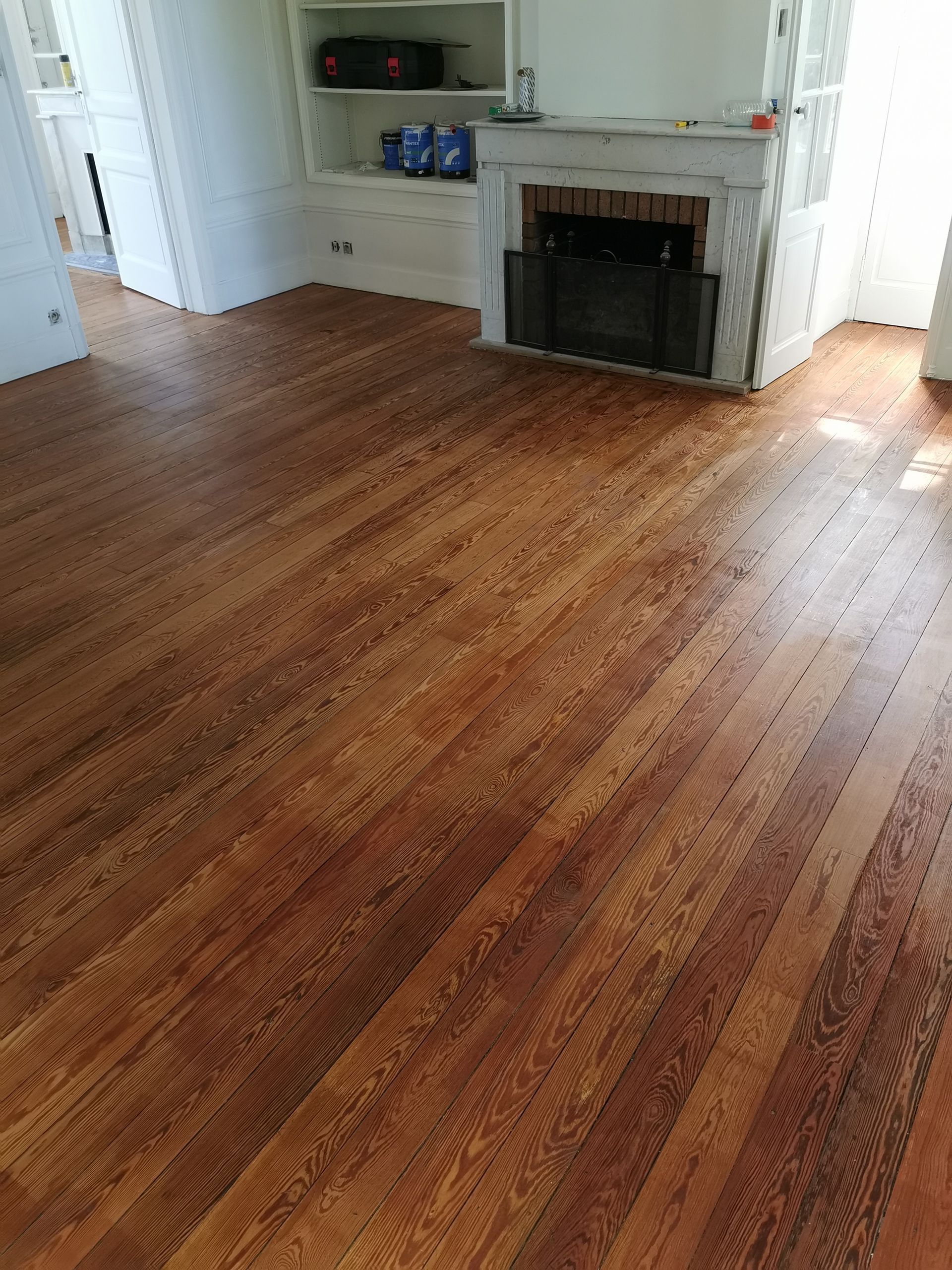 Sol en bois dans une pièce, avec une cheminée et des étagères encastrées en arrière-plan.