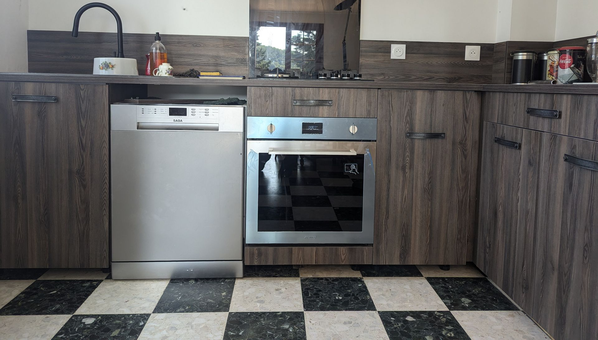 Cuisine avec lave-vaisselle et four encastrés dans des placards en bois, sol à damier.