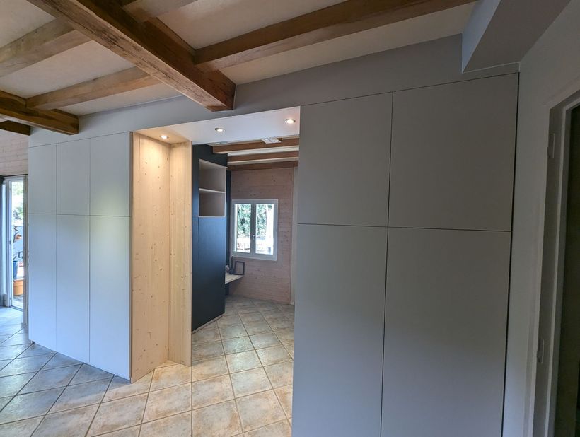 Vue intérieure d'une pièce avec des placards clairs, des poutres en bois et un sol carrelé.