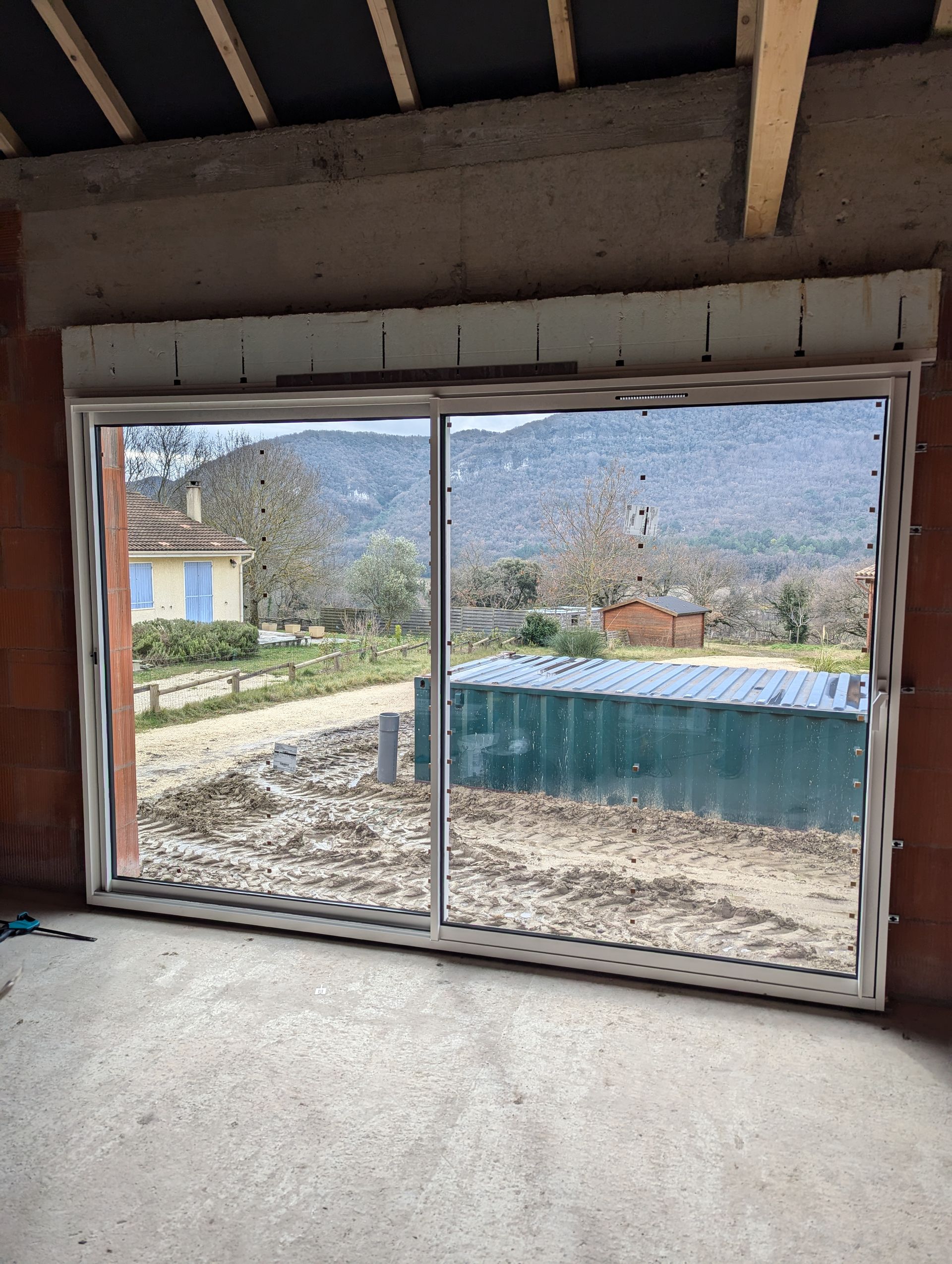 Porte coulissante en verre, avec un volet roulant au-dessus, offrant une vue panoramique sur un paysage de bâtiments et de montagnes.
