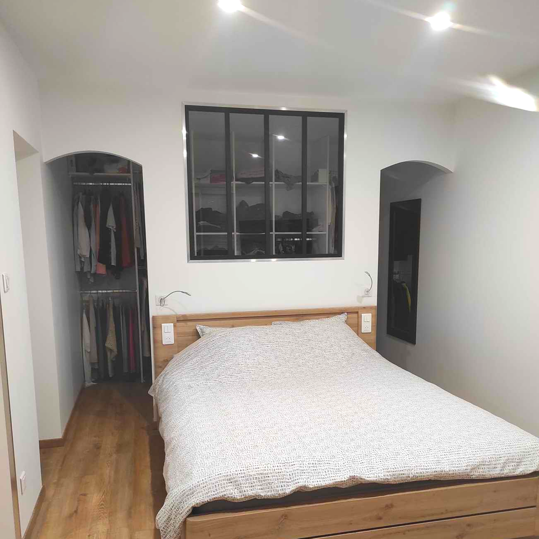 Petite chambre avec un lit, des placards ouverts et une fenêtre au-dessus de la tête de lit.
