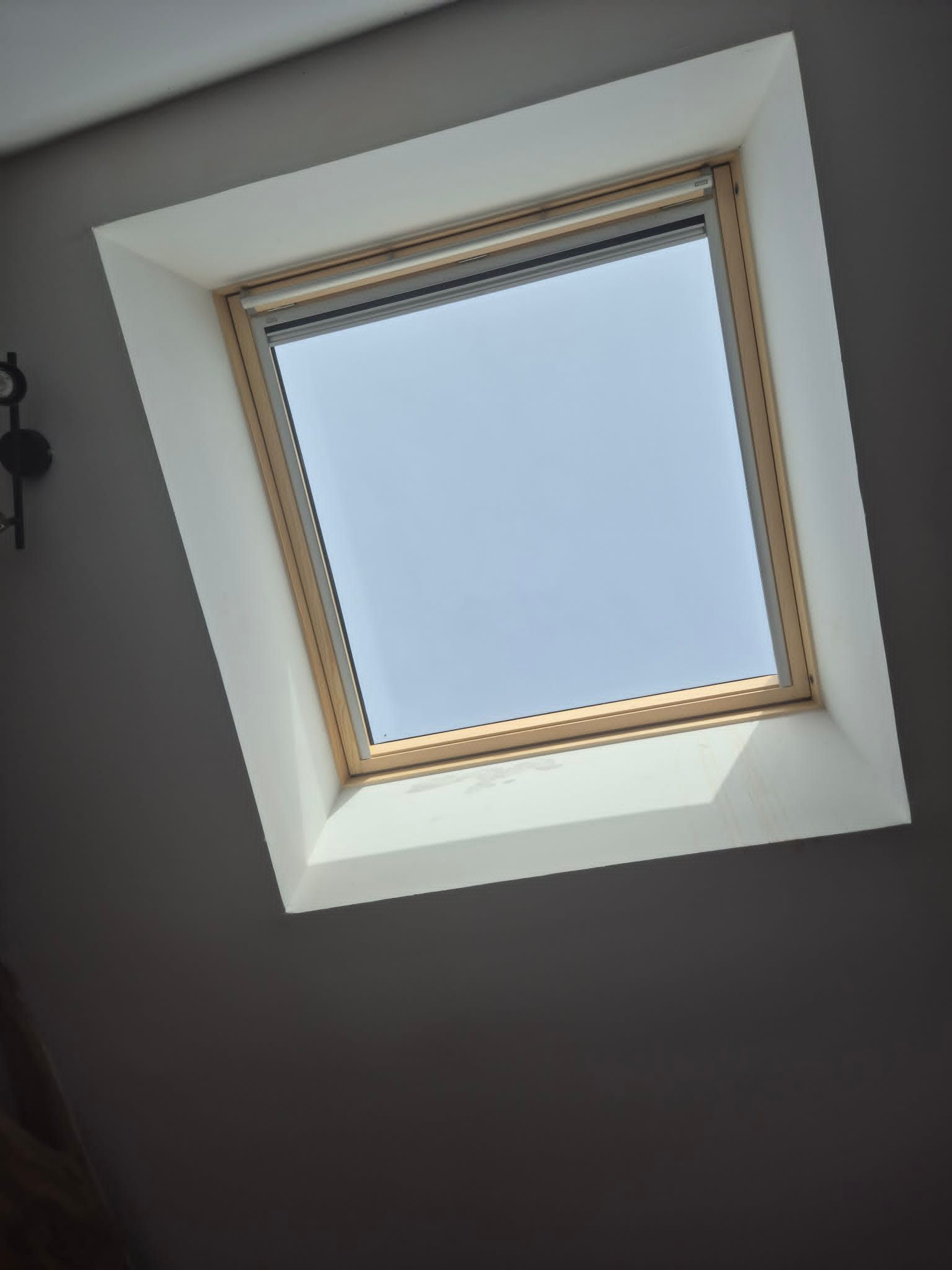 Vue inclinée d'une fenêtre de toit avec un ciel bleu pâle et un cadre de plafond blanc