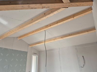 Plafond intérieur avec poutres en bois apparentes et câble noir suspendu dans une pièce blanche.