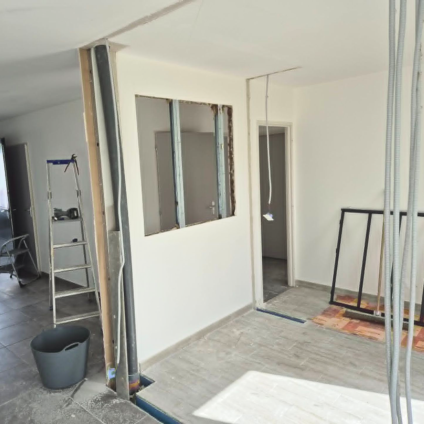Pièce partiellement rénovée avec montants apparents, une échelle, une poubelle et une porte en construction
