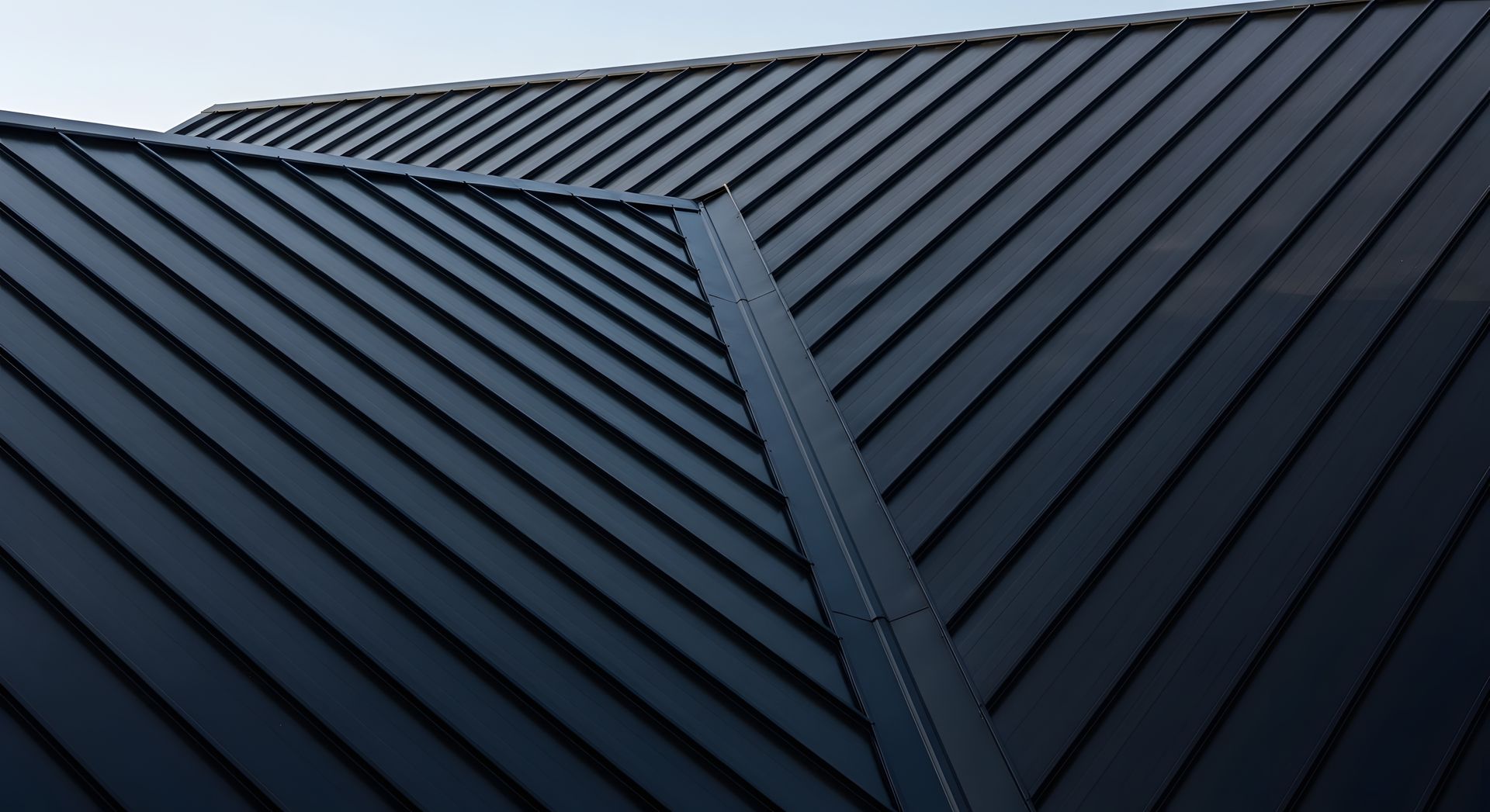 Panneaux de toiture en métal sombre à joints debout avec une arête centrale sous un ciel gris