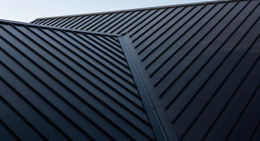 Panneaux de toiture en métal sombre à joints debout avec une arête centrale sous un ciel gris