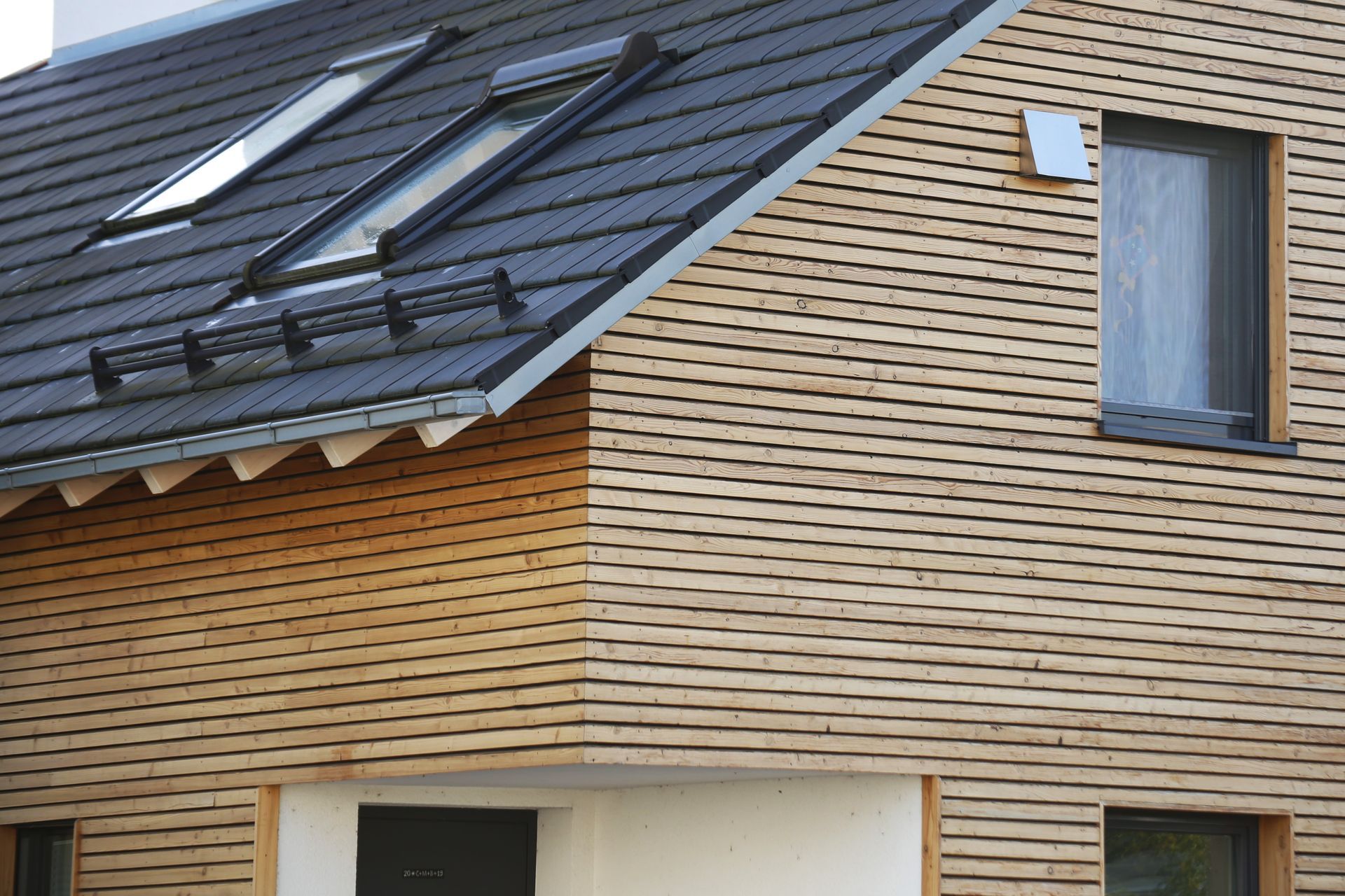 Extérieur de maison moderne avec toit foncé, bardage en bois clair et petite fenêtre