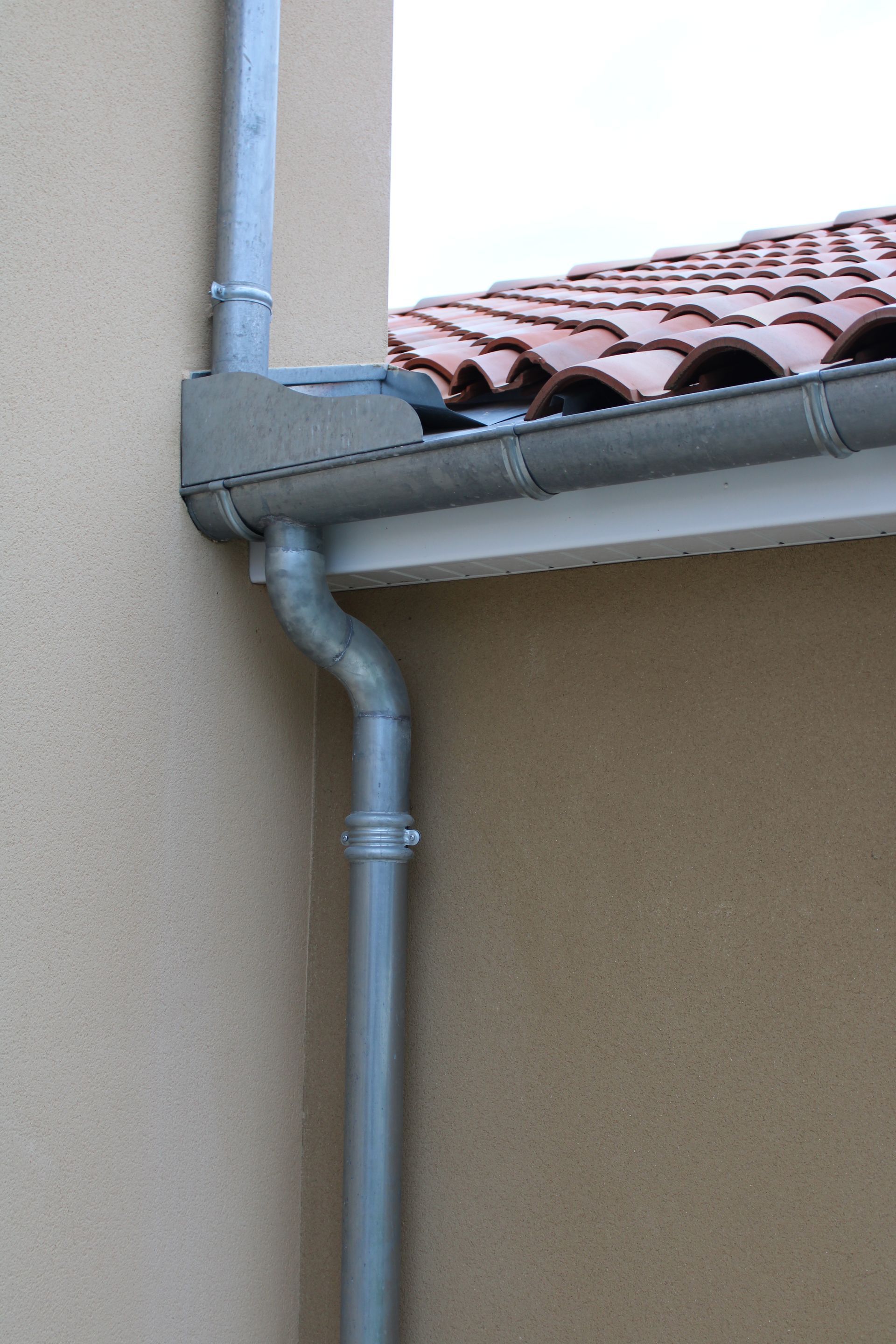 Gouttière et descente pluviale sur une maison avec un toit de tuiles rouges et un mur beige