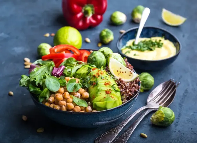 A bowl of healthy food with avocado , chickpeas , brussels sprouts and quinoa.