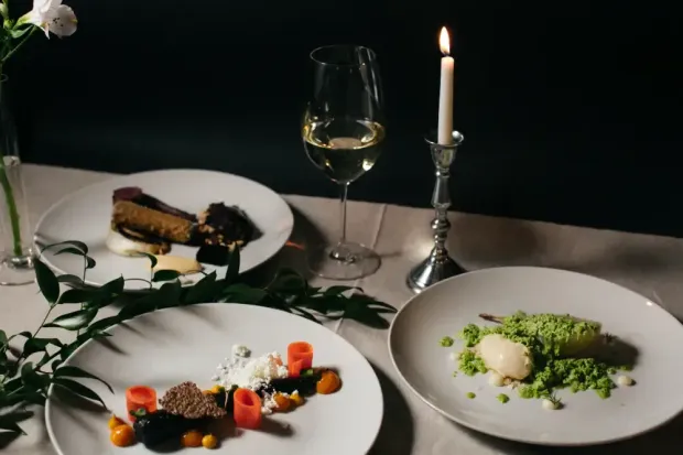 There are three plates of food and a glass of wine on the table.