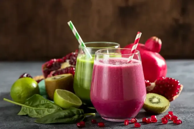 Three smoothies in glasses with straws and fruit on a table.