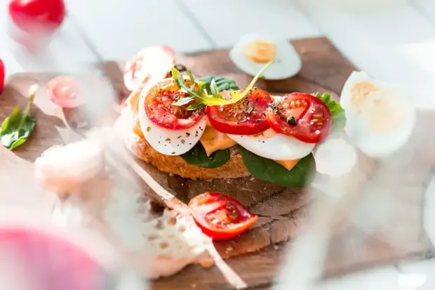 A close up of a sandwich with tomatoes and hard boiled eggs on a wooden cutting board.