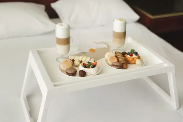 There is a tray of food and drinks on the bed.